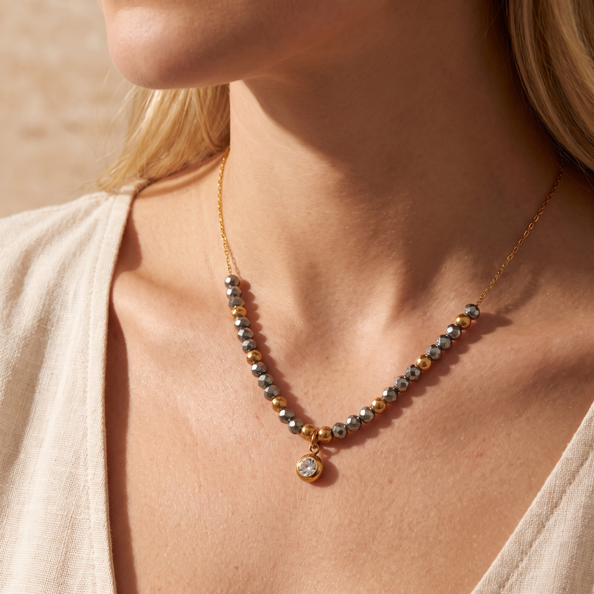 Model wearing a gold-tone beaded necklace with dark gray faceted beads against a light beige top.