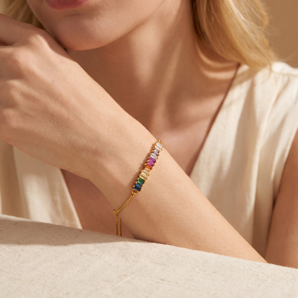Model resting her arm while wearing the gold-tone rainbow baguette bracelet.
