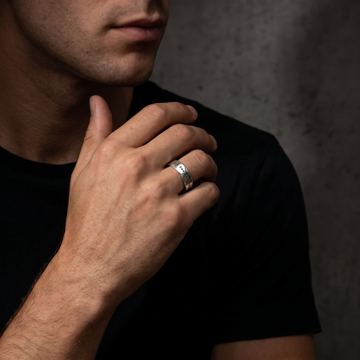 Model wearing the silver stamped ring on his ring finger against a black shirt and dark background.