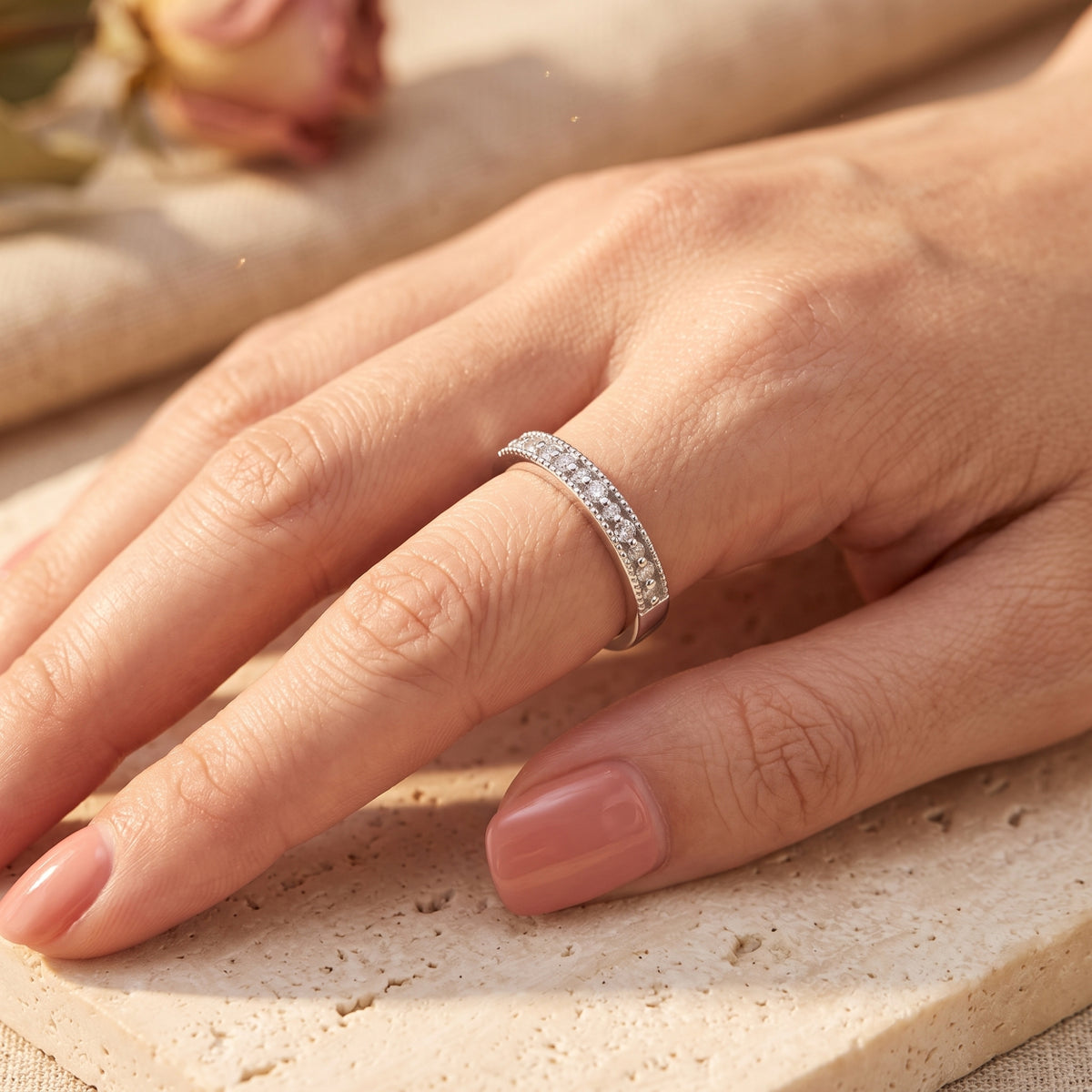 Angled view of a hand wearing the silver milgrain band ring resting on a beige stone surface.