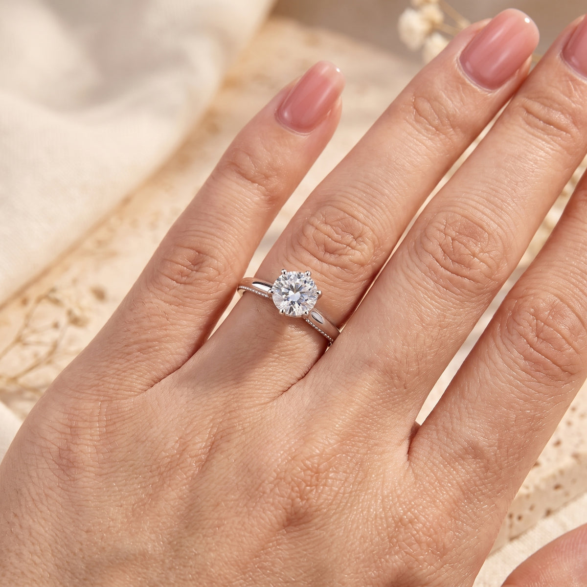 Close-up view of the silver round-cut ring worn on a hand, highlighting its brilliant stone and milgrain band.