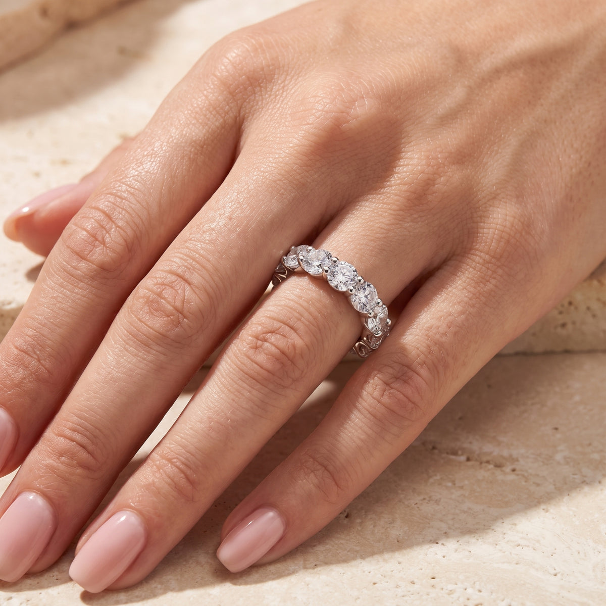 Angled overhead view of a hand wearing a silver shared-prong eternity ring with round clear stones.