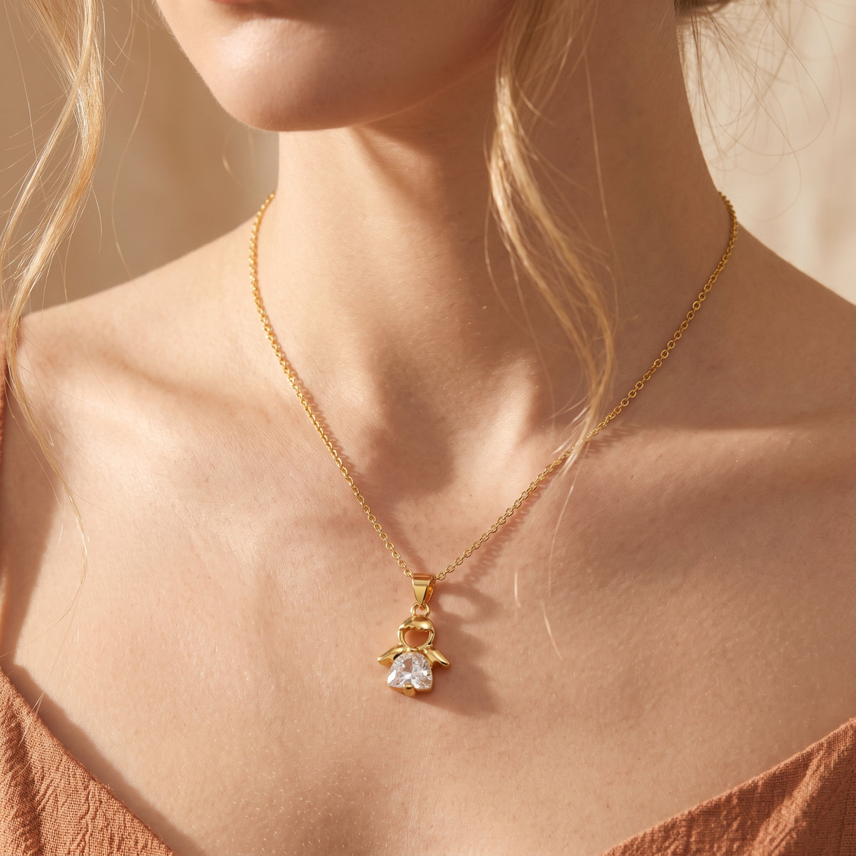 Front view of a woman wearing the gold-tone angel pendant necklace against a warm-toned top.