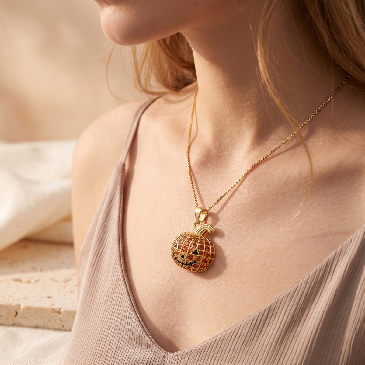 Model wearing the gold-tone pumpkin pendant necklace with a sleeveless taupe top.