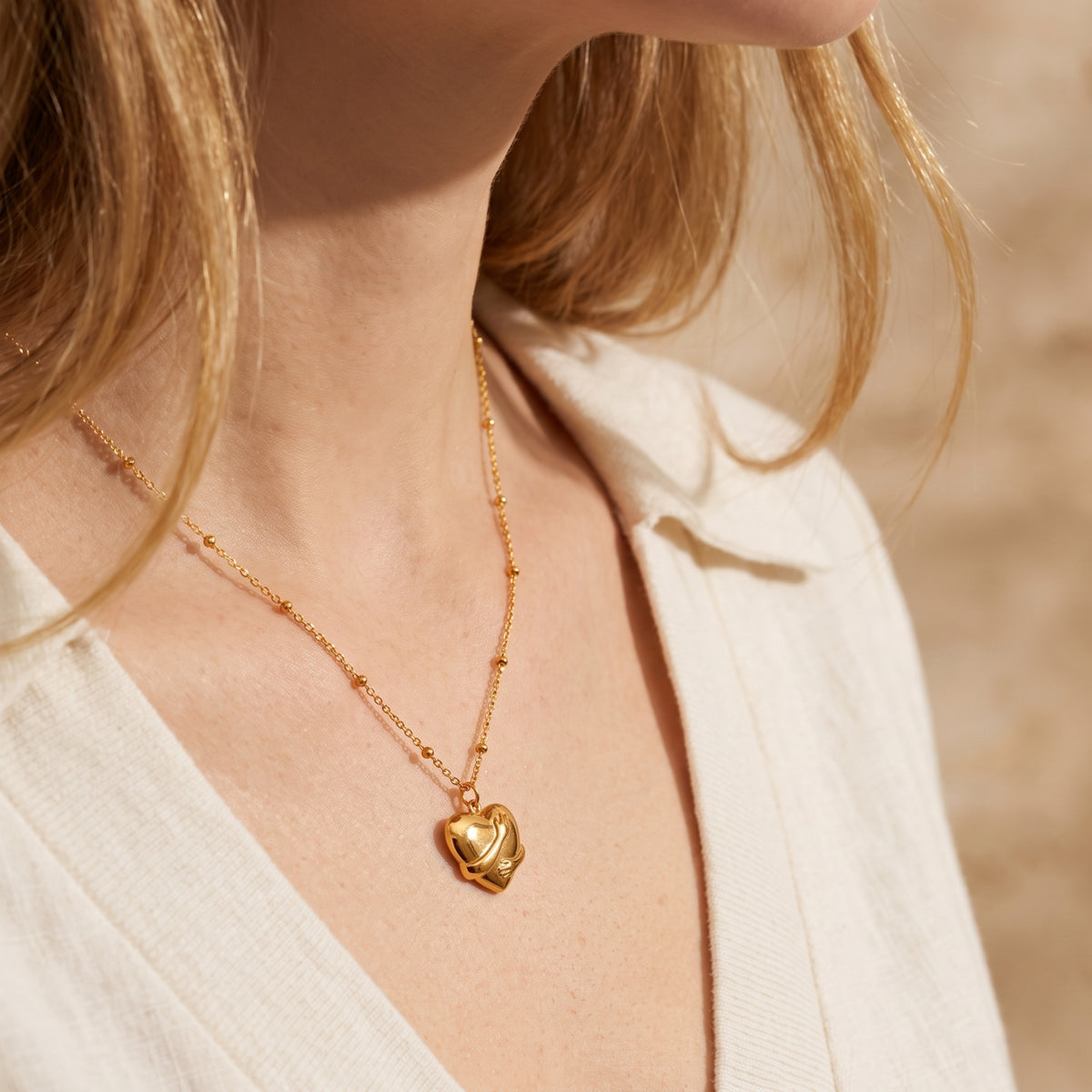 Side-angle view of a woman wearing the gold-toned hugging heart pendant necklace with a white shirt.