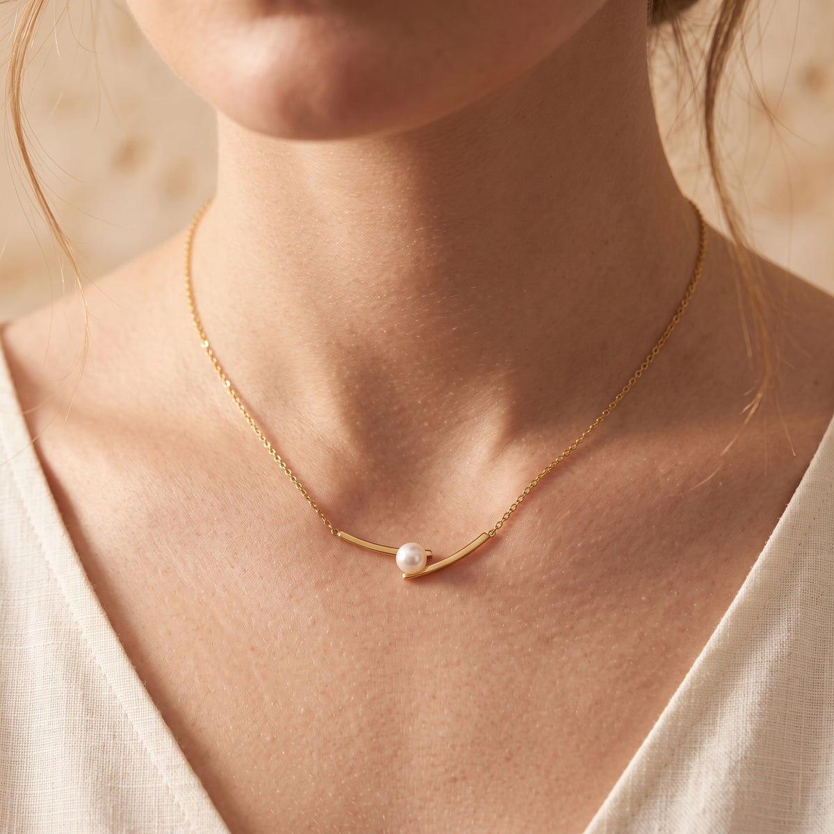 Front close view of a model wearing the gold-tone arc bar necklace with an offset white pearl