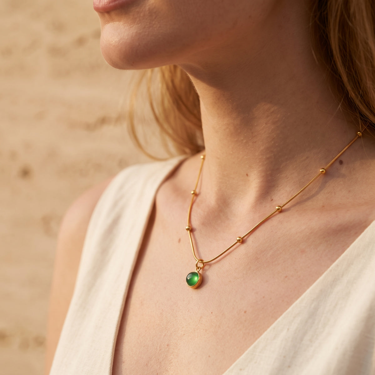 Angled on-model view of a gold-tone snake chain necklace with sphere stations and round green cabochon pendant.