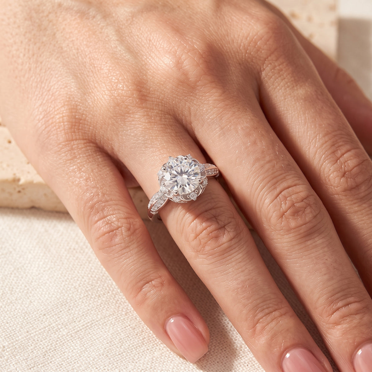 Close-up hand view of the silver floral solitaire ring worn on a ring finger against a soft fabric backdrop.