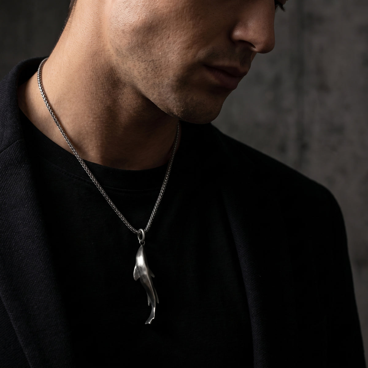 Man wearing a silver shark pendant necklace over a black shirt and dark jacket