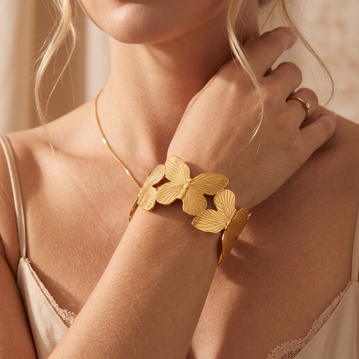 Model wearing the gold-tone butterfly cuff bracelet with her wrist raised near her neck.