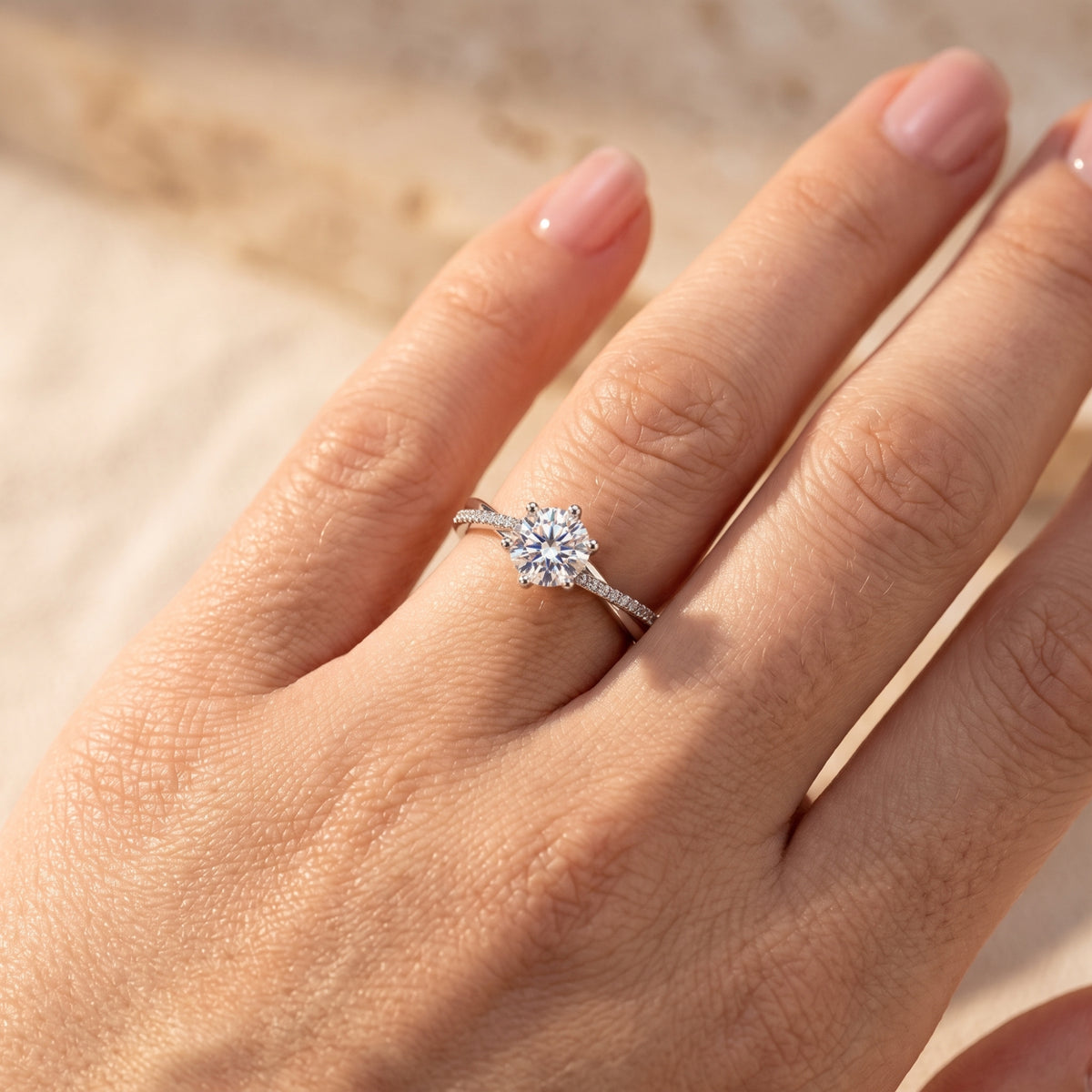 Close-up of a silver crossover ring with a round clear center stone worn on a finger in warm light.