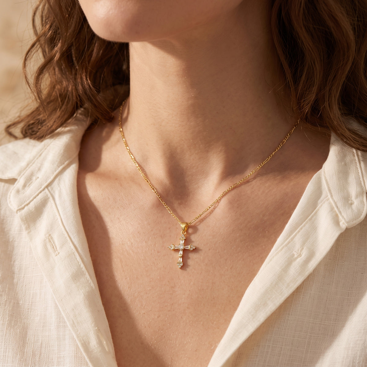 Model wearing the gold-tone cross necklace with an open white button-down shirt.