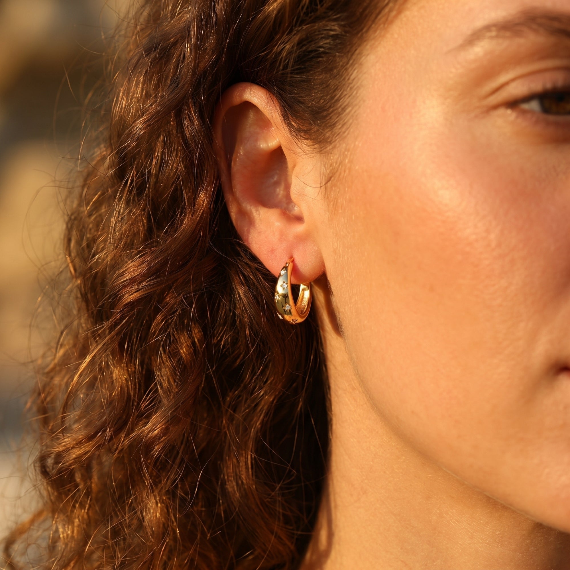 Side view of a gold starburst huggie hoop earring with sparkling accents worn by a model.
