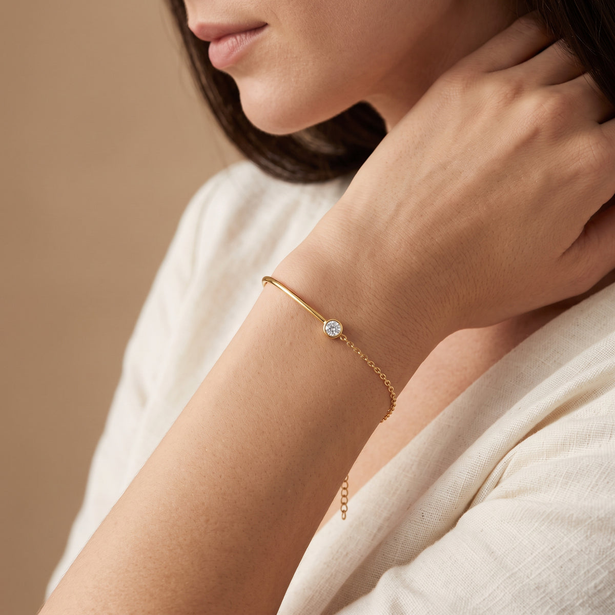 Model wearing the gold-tone bezel station cuff bracelet, shown with her hand near her wrist and lower face visible.
