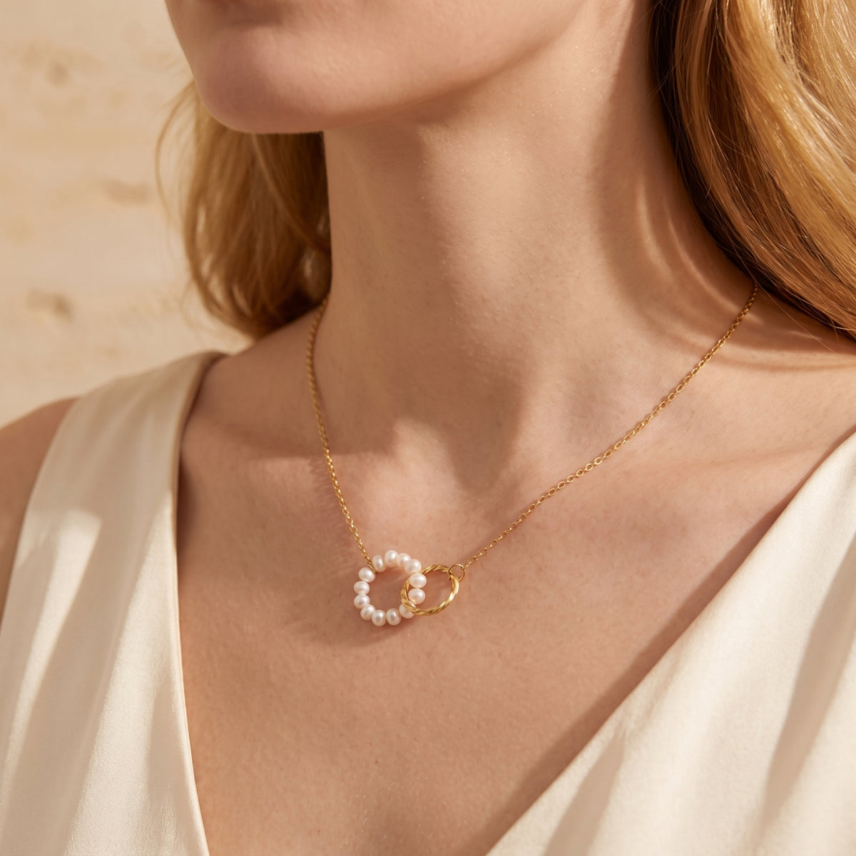 Close-up of a model wearing the gold-tone necklace with pearl circle and twisted ring pendant over a white garment.
