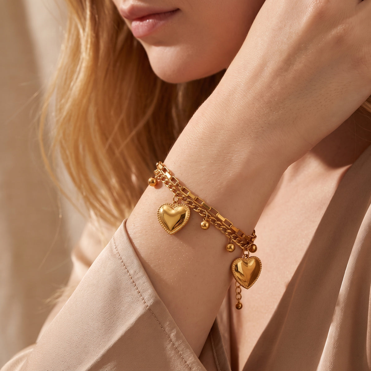 Model wearing the gold-tone double-chain bracelet, showing two heart charms and bead drops draping from the wrist.