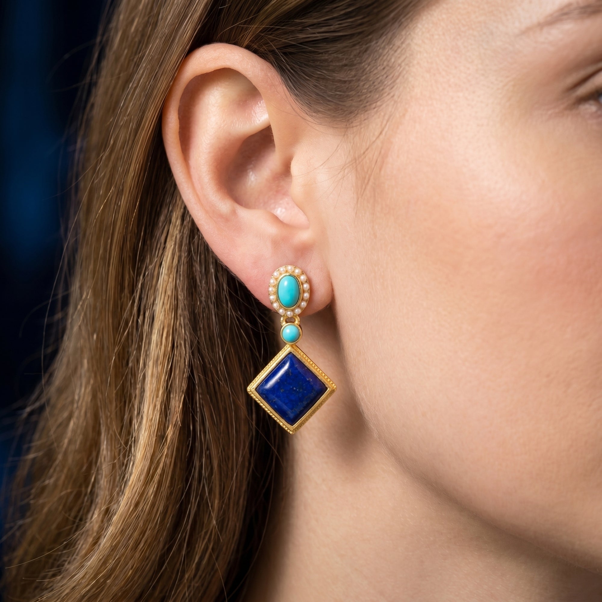Side view of the Azure Rhombus natural lapis lazuli and turquoise gold plated earrings worn on a model's ear.