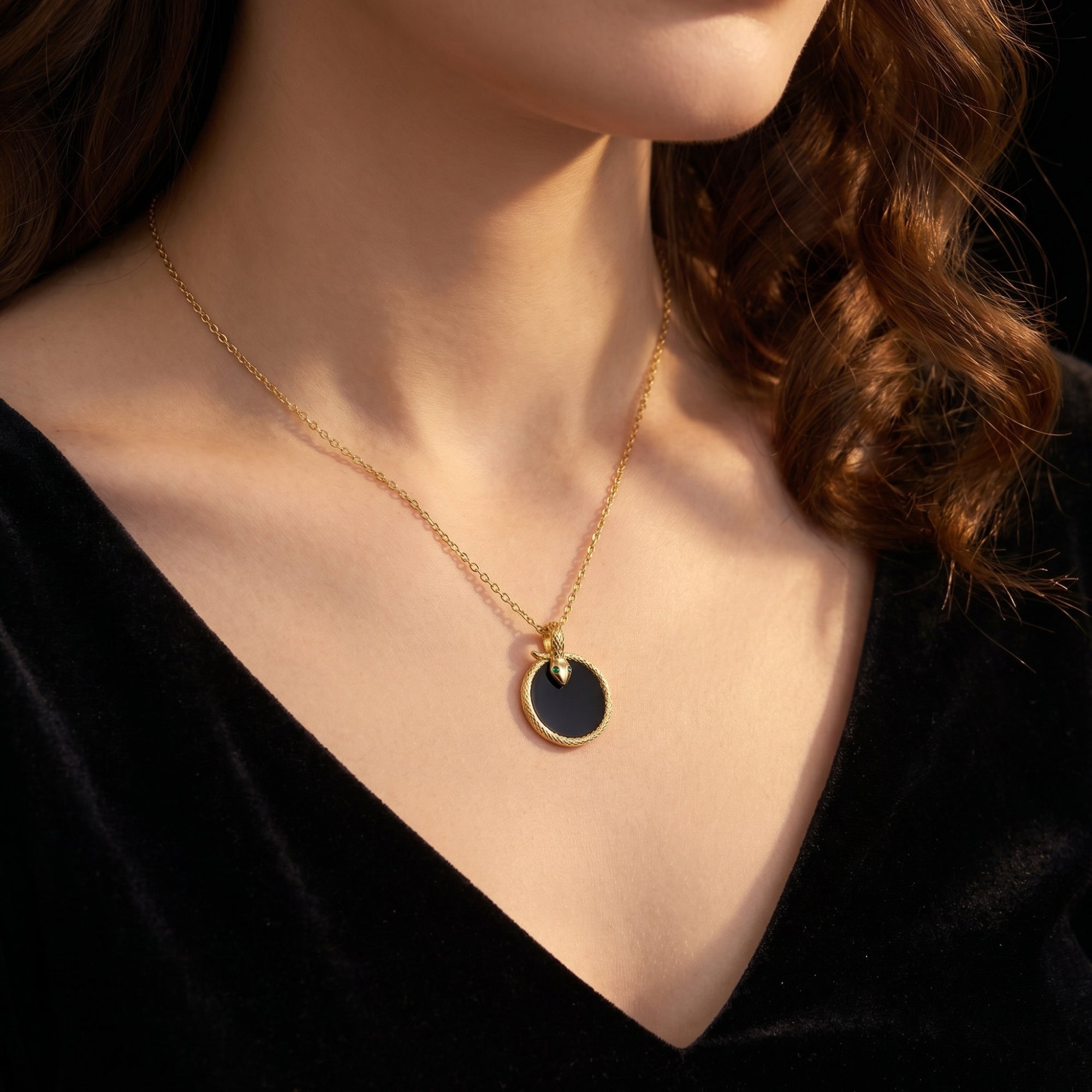 Gold Polaris snake necklace with round black onyx pendant worn by a model in a black dress.