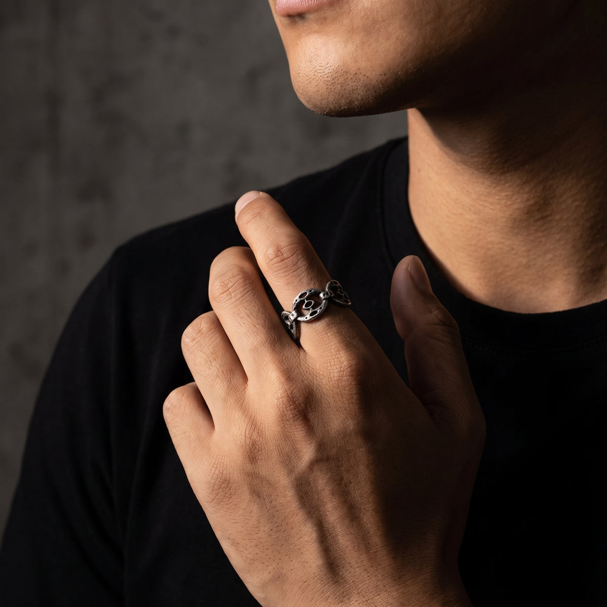 Man in a black shirt holding his hand near his face while wearing the distressed silver oval-link ring.