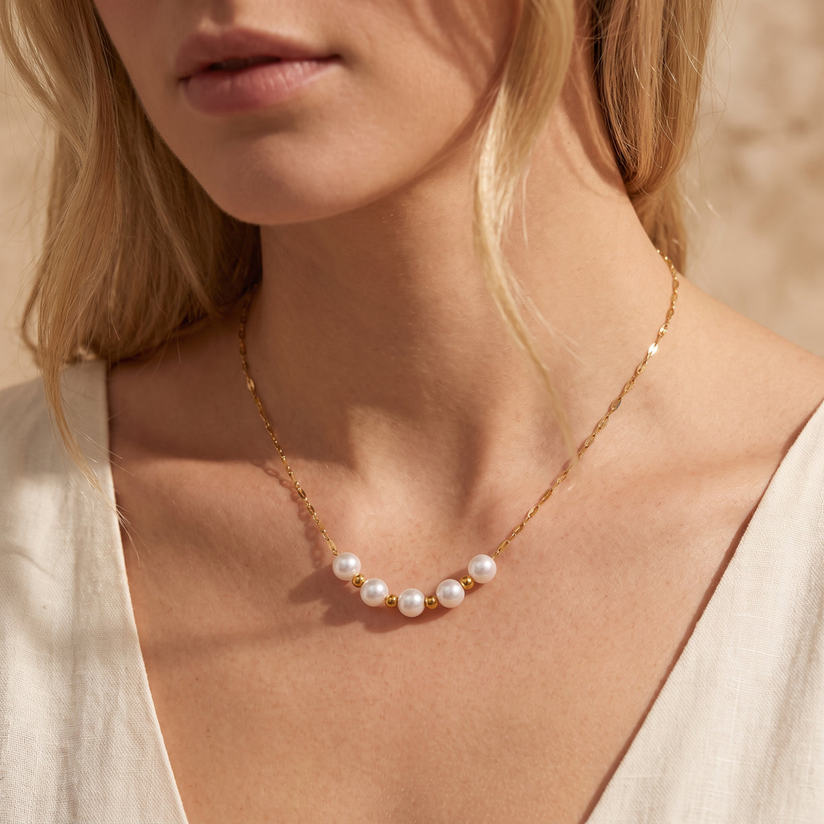 Front view of a woman wearing the gold-tone chain necklace featuring white pearls and gold-tone spacer beads.