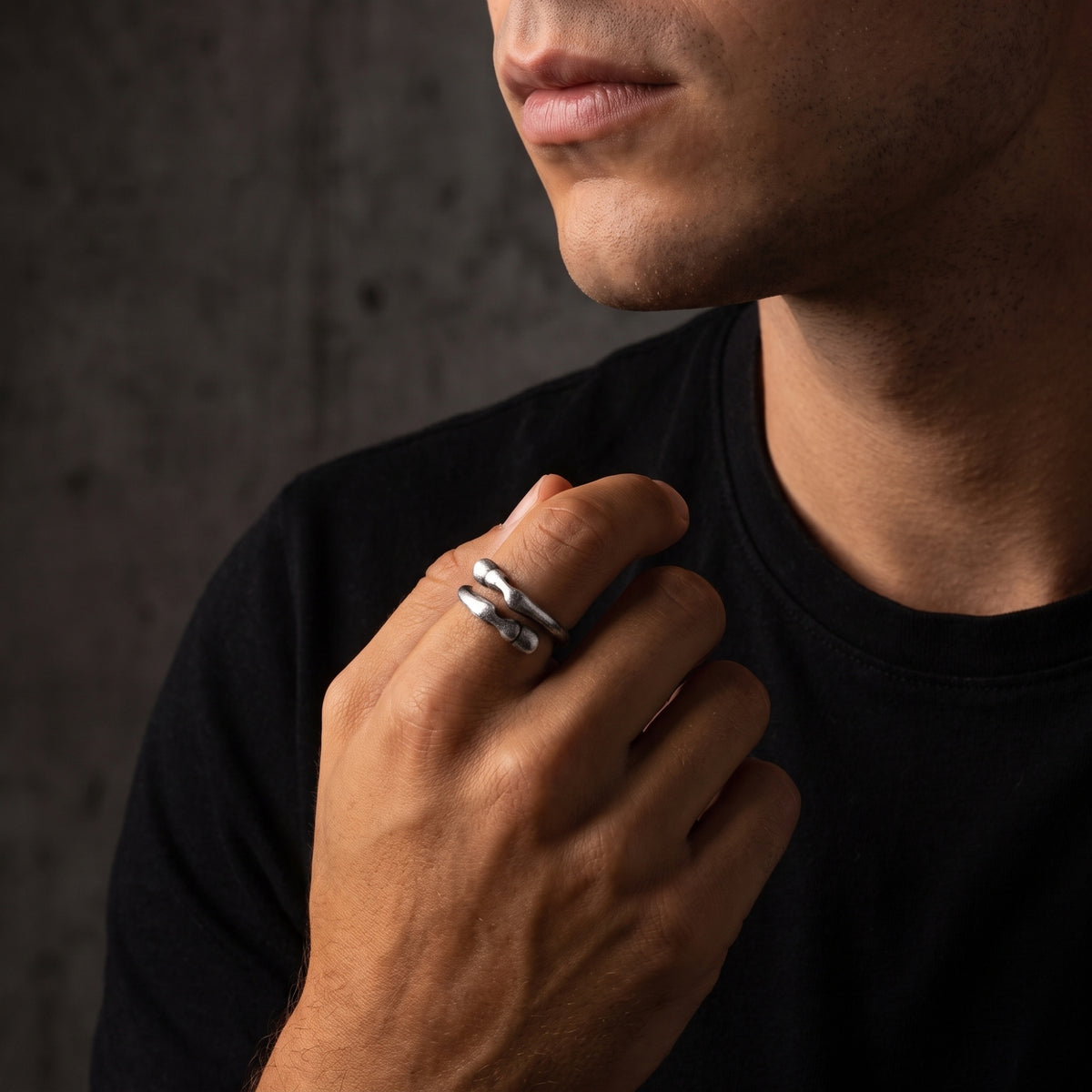 Model wearing a sculpted 999 fine silver open-band ring against a black T-shirt, shown near the face.