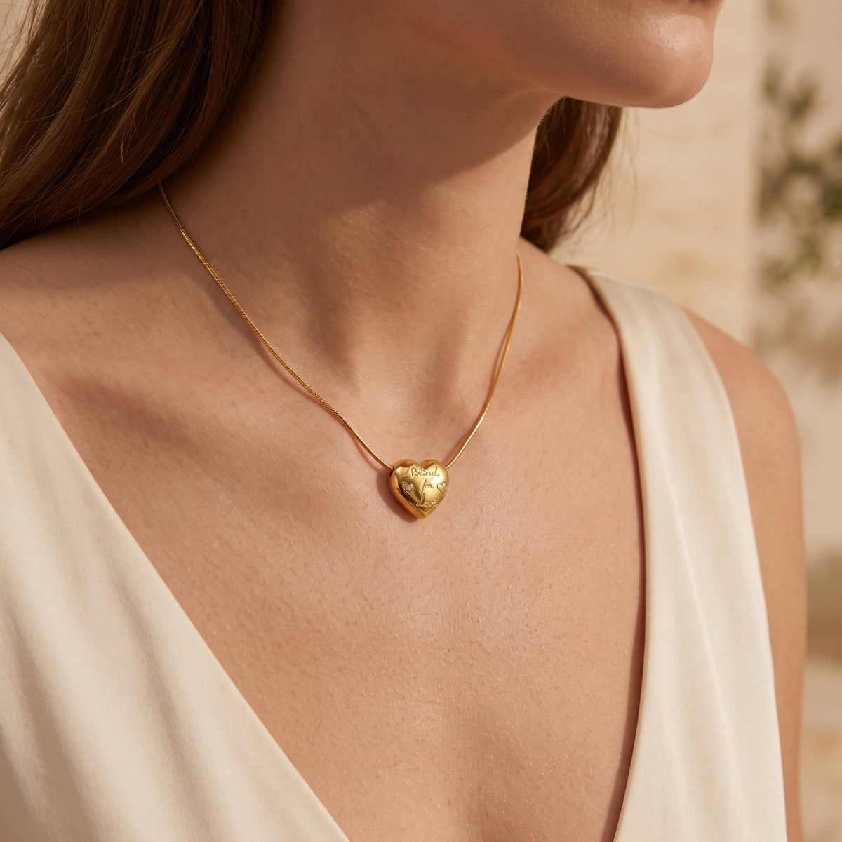 Model wearing the gold-tone engraved puffed heart pendant necklace with a white sleeveless dress.