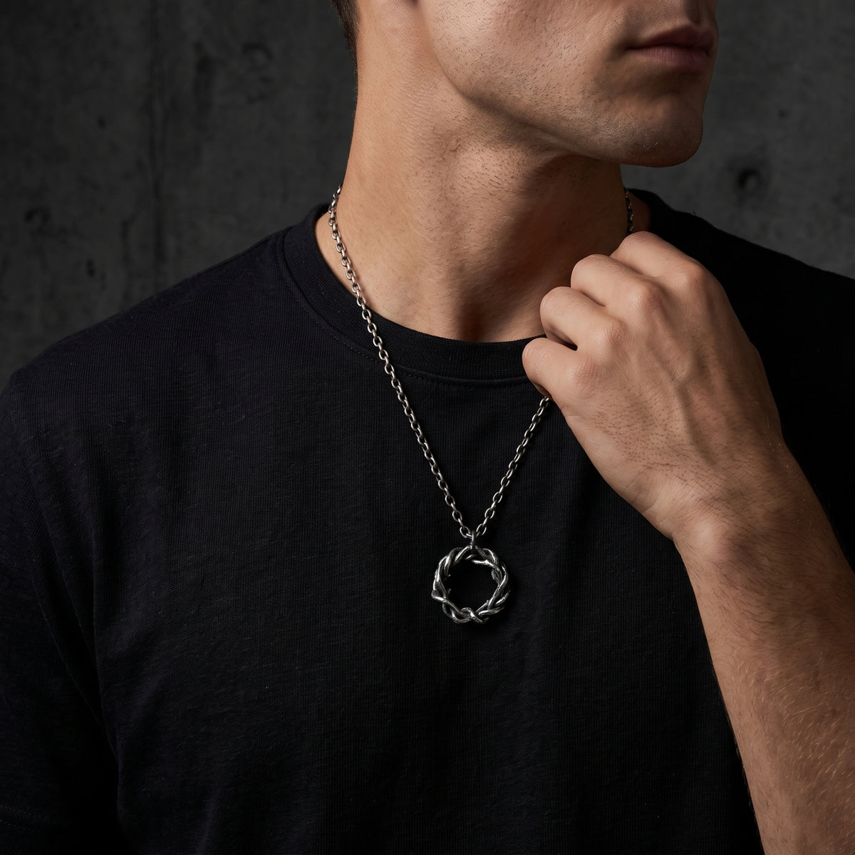 Man wearing the intertwined silver circular pendant over a black T-shirt while holding the chain near his collar.