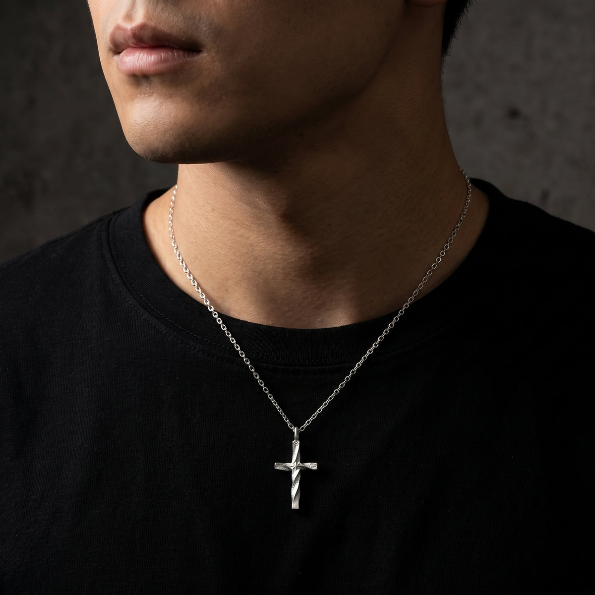 Front-facing close-up of a man wearing the silver twisted cross necklace over a black T-shirt.