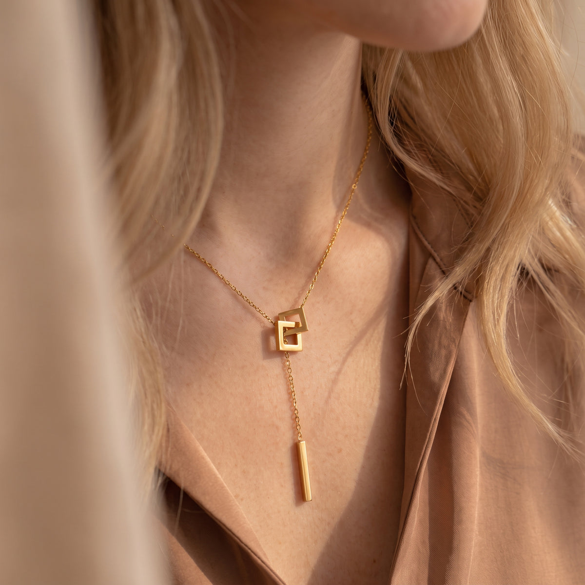 Close-up of the gold-color square link lariat necklace styled on a model wearing a neutral blouse.