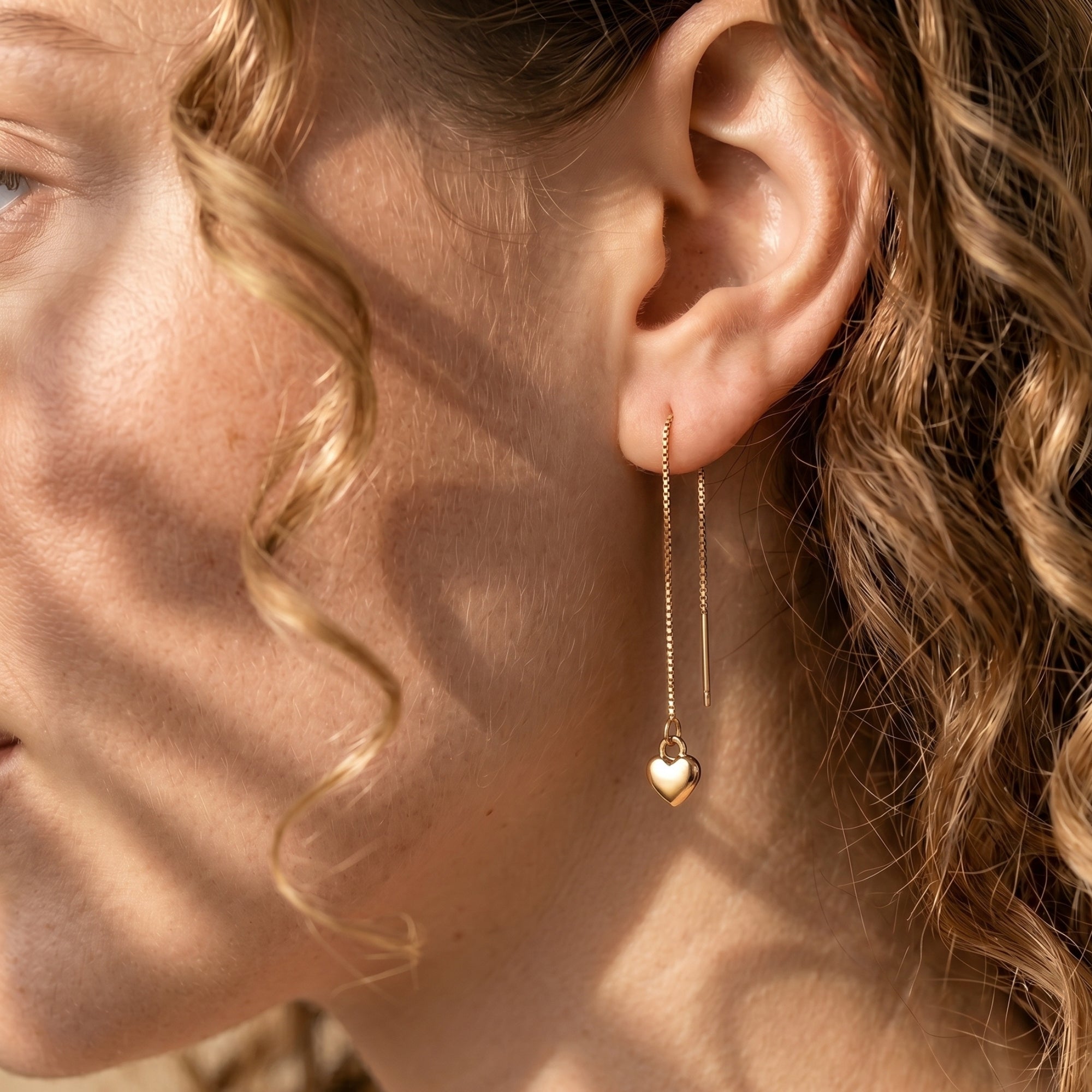 Side view of a model wearing a gold heart threader earring, highlighting the elegant drape of the box chain.