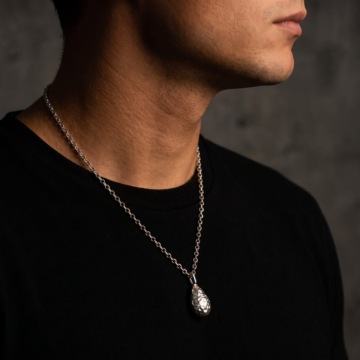 Side-profile view of a person wearing the textured silver teardrop pendant on a link chain.