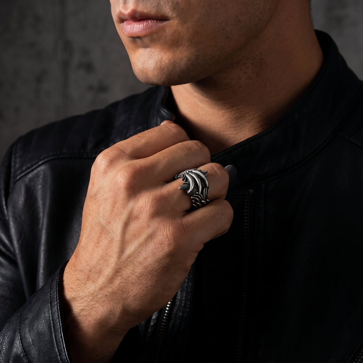 Close-up of a man wearing the textured silver feather ring on his middle finger near a black jacket collar.