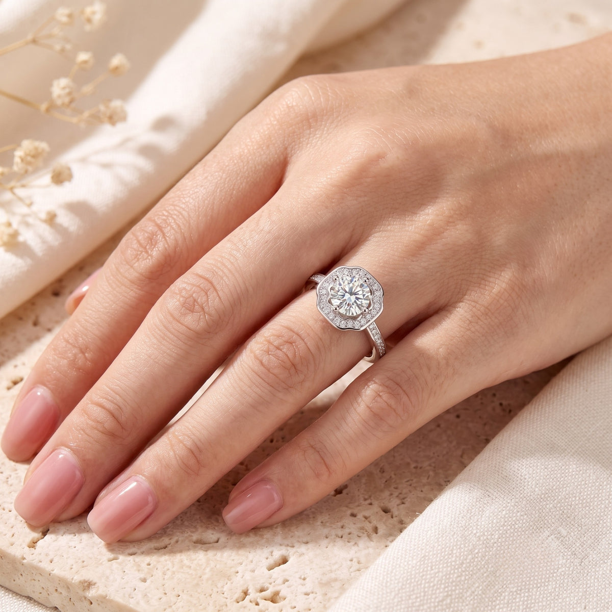 A hand wearing the silver scalloped halo ring on a light stone surface.