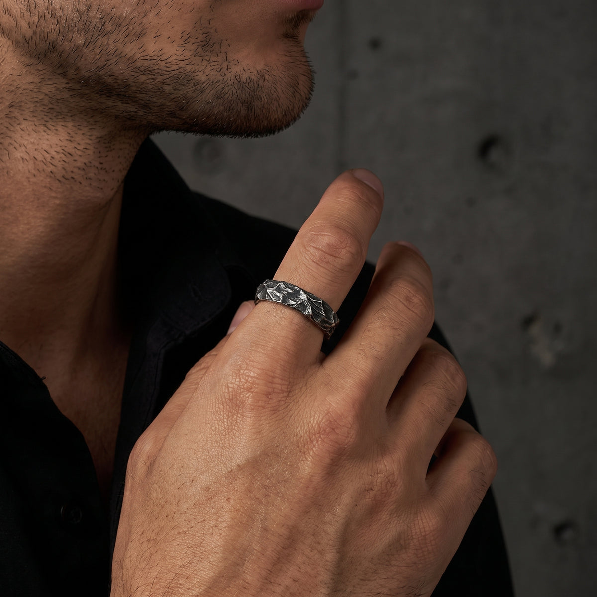 Profile view of a man wearing the carved silver open-band ring on his index finger against a dark backdrop.