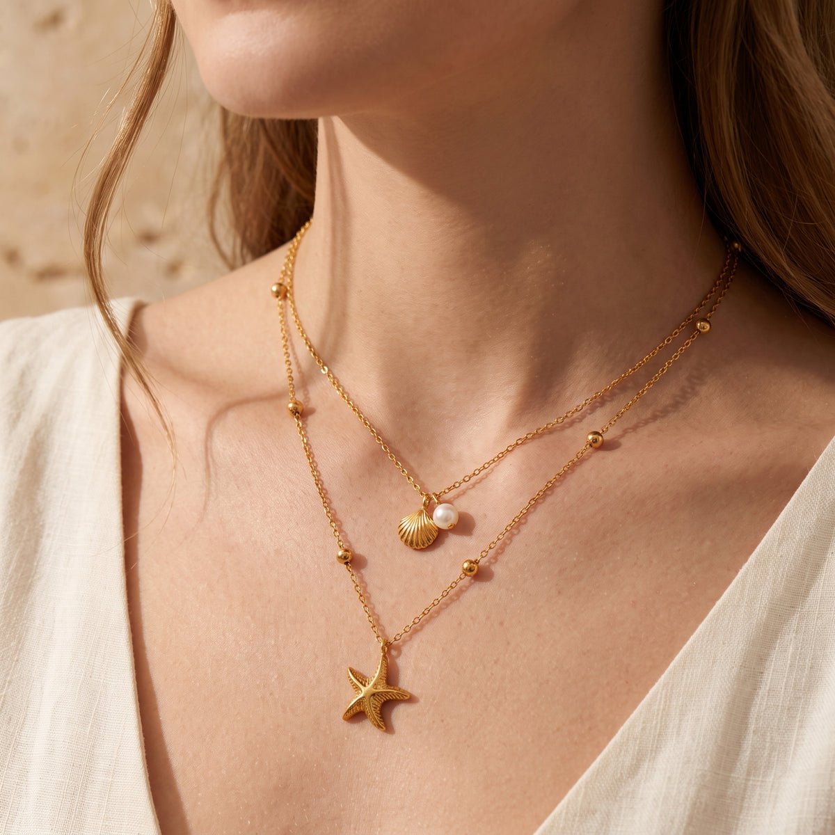 Close-up on-model view of the gold-tone layered necklace with shell, simulated pearl, and starfish charms.