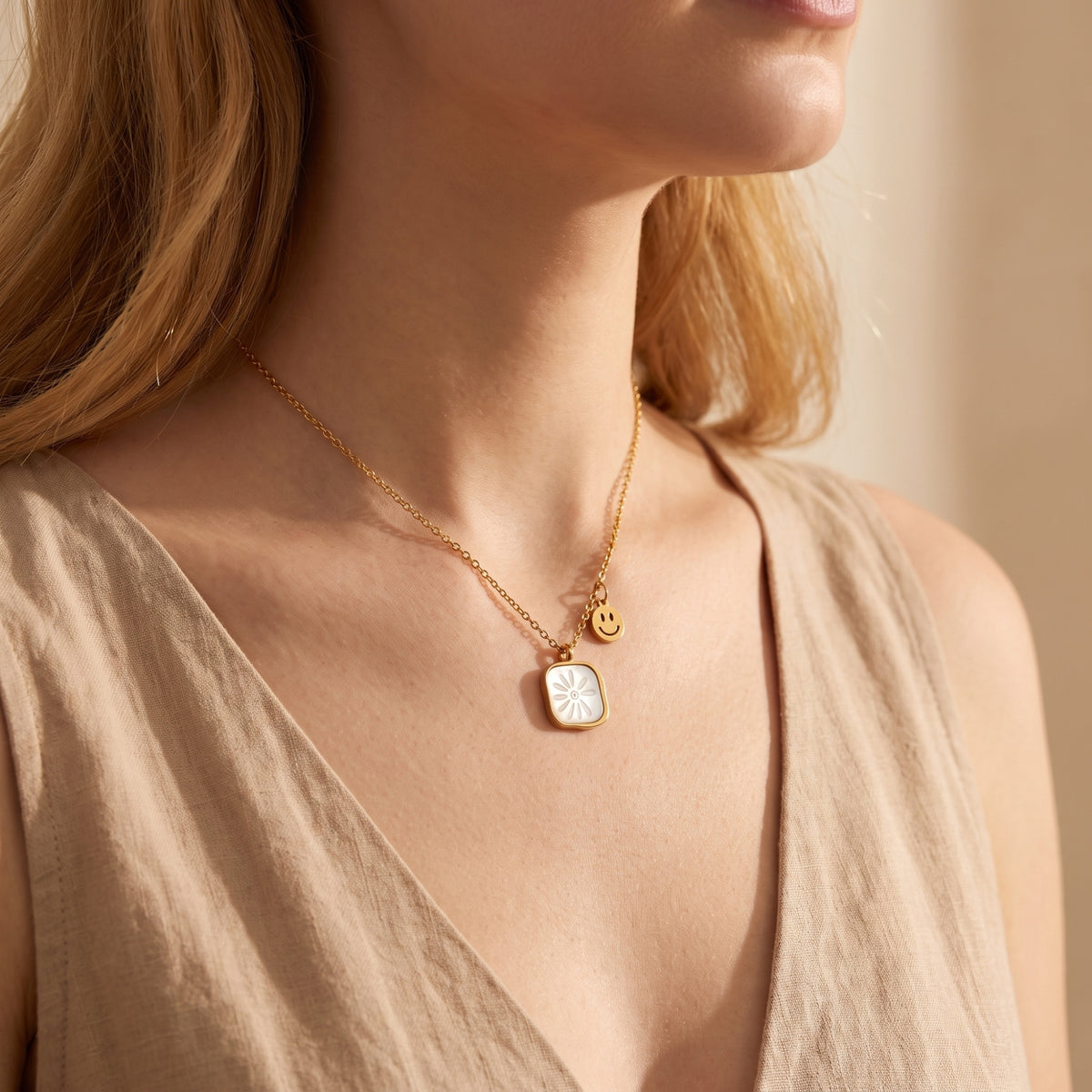 Model wearing the daisy shell pendant necklace with a gold smiley-face charm over a cream sleeveless top.