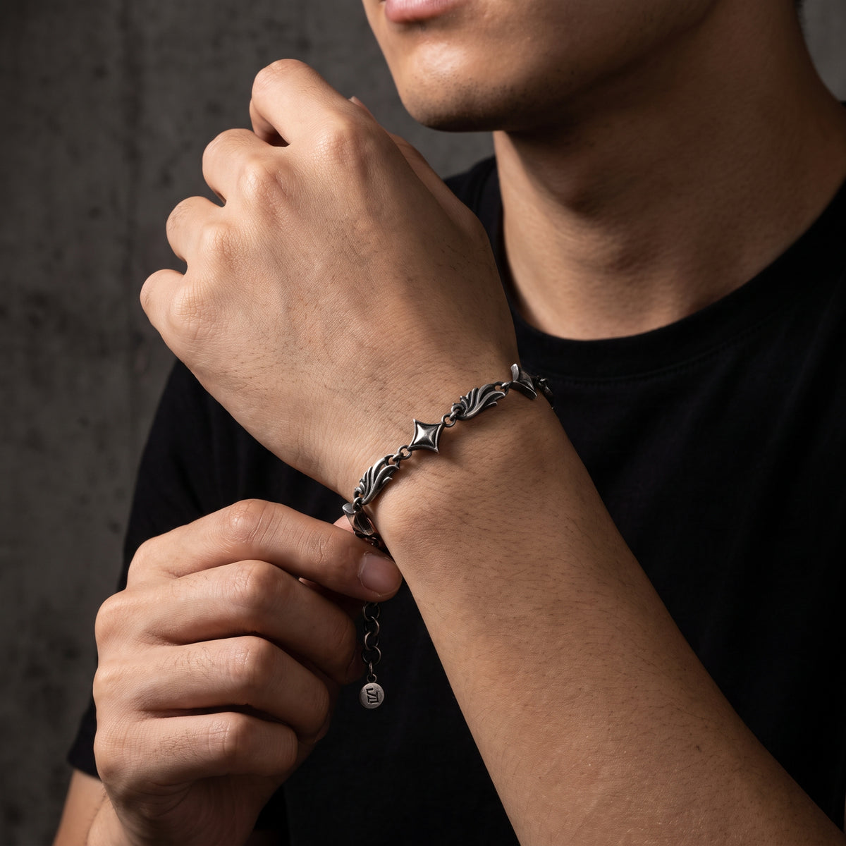 Model adjusting the silver star link bracelet at his wrist with his opposite hand and extension chain visible.