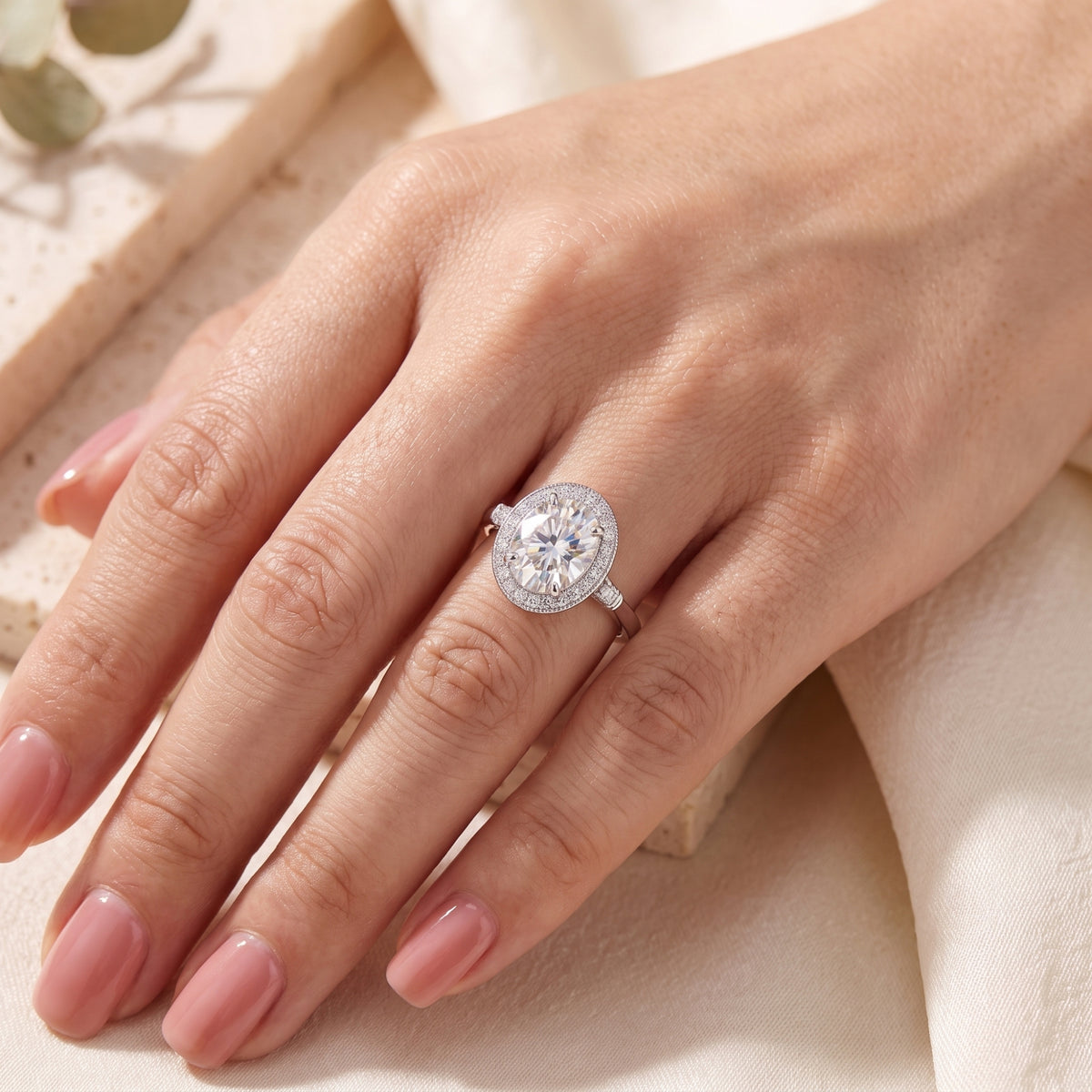 Top view of the silver oval halo ring worn on a finger against a warm neutral backdrop.