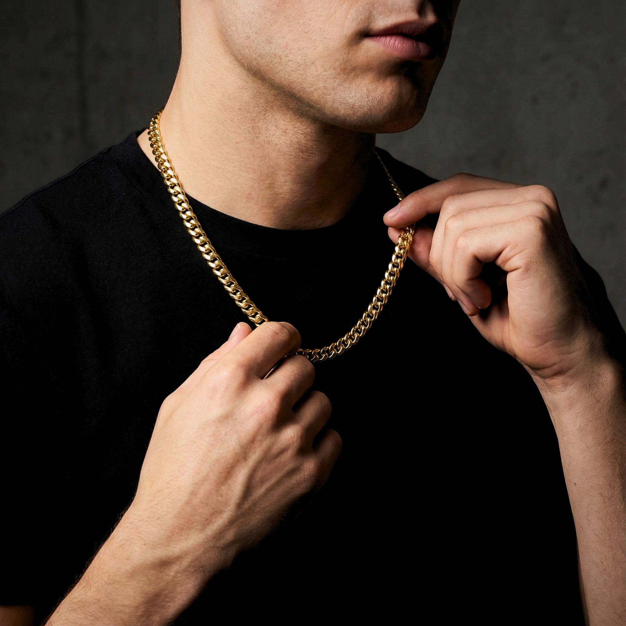 Close-up of a man's hands adjusting a 6mm gold Cuban chain around his neck.