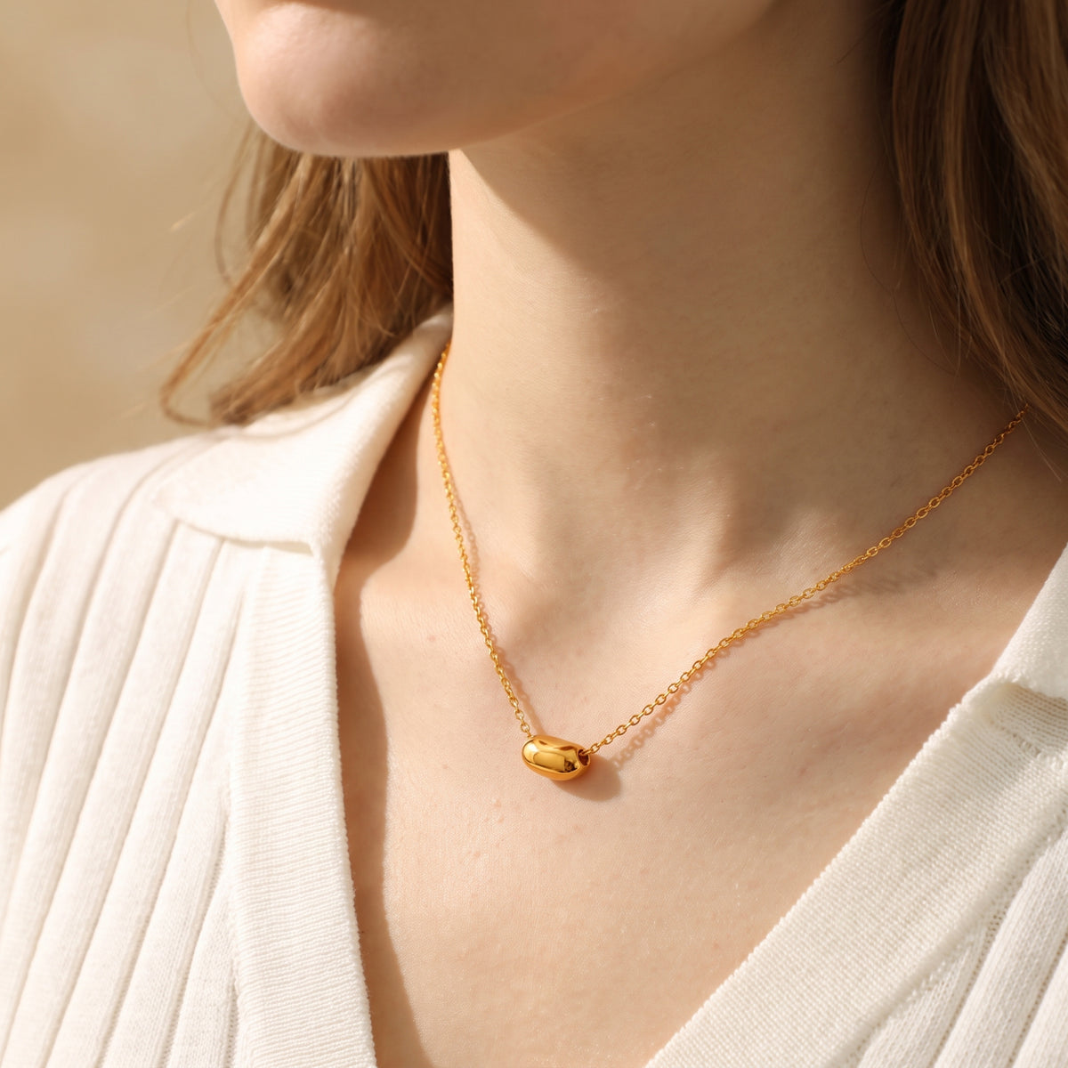 Model wearing the gold-toned sculpted pod necklace over a white ribbed knit top.