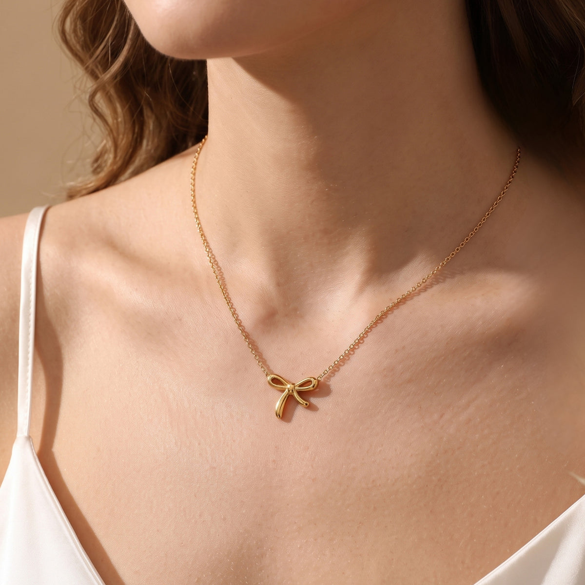 Model wearing the gold-tone bow pendant necklace with a white camisole.