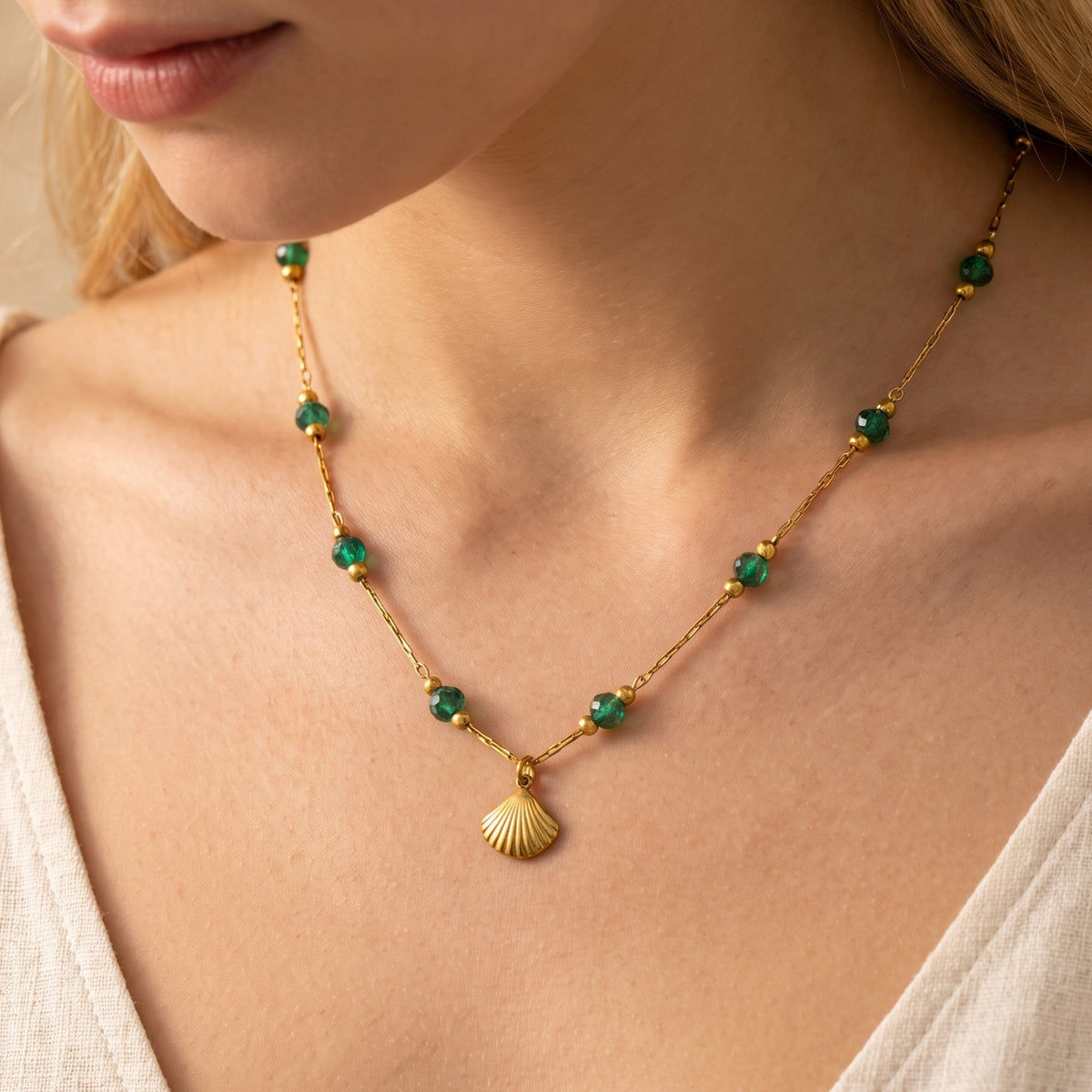 Front close-up of the gold-tone shell necklace with green crystal beads worn over a white neckline.