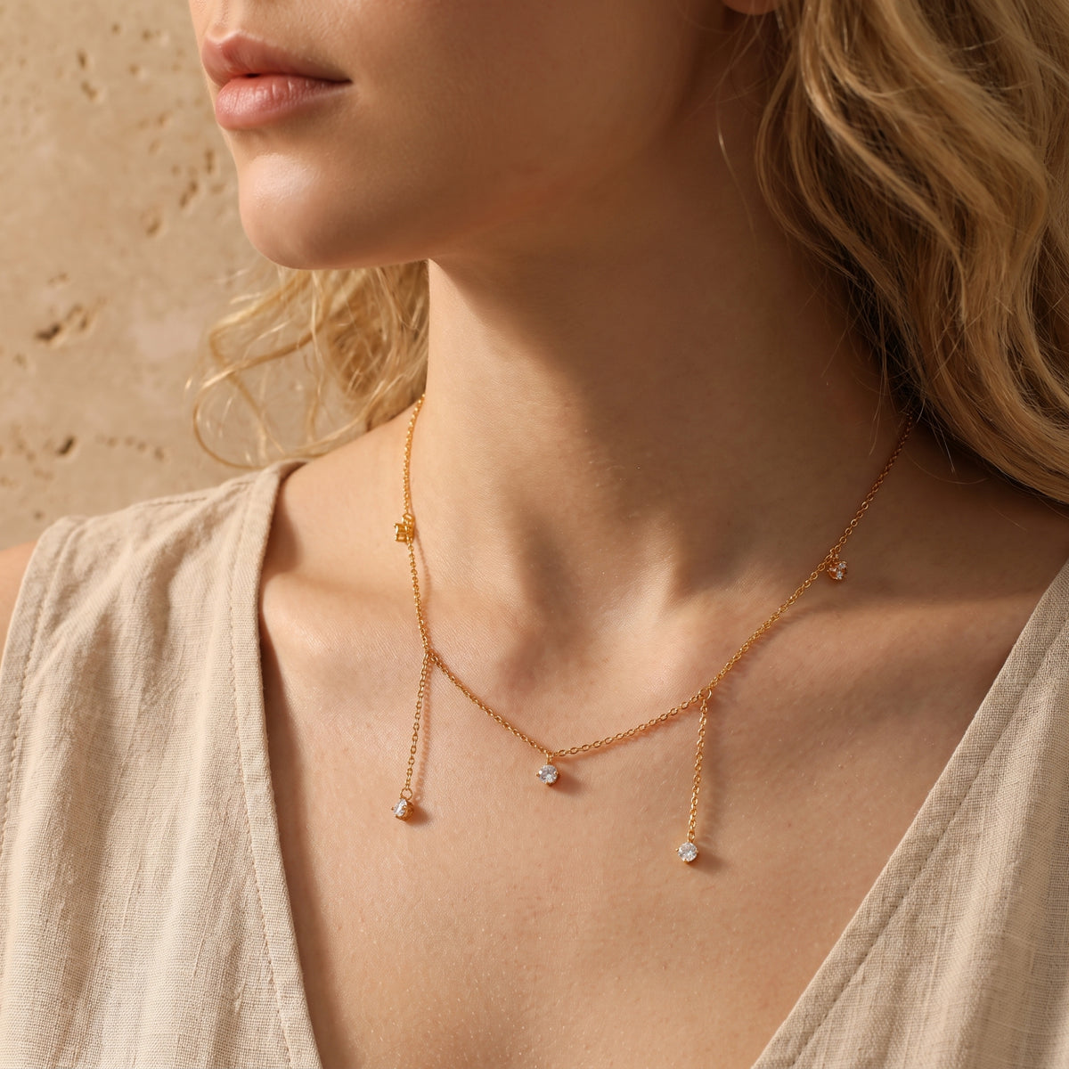 Model wearing a gold-tone five-drop necklace with clear stones over a beige top in close-up.