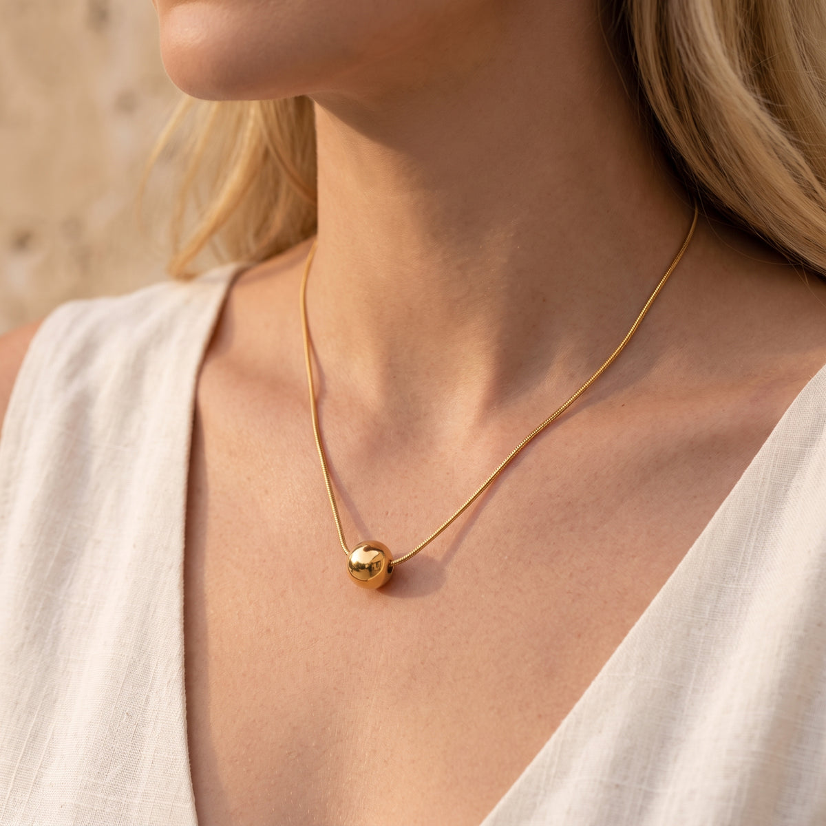 Angled close-up of a model wearing the gold-tone sphere necklace over a white top.