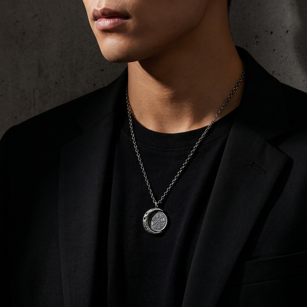 Model wearing the silver lunar coin pendant necklace over a black shirt and blazer, with the pendant at mid-chest.