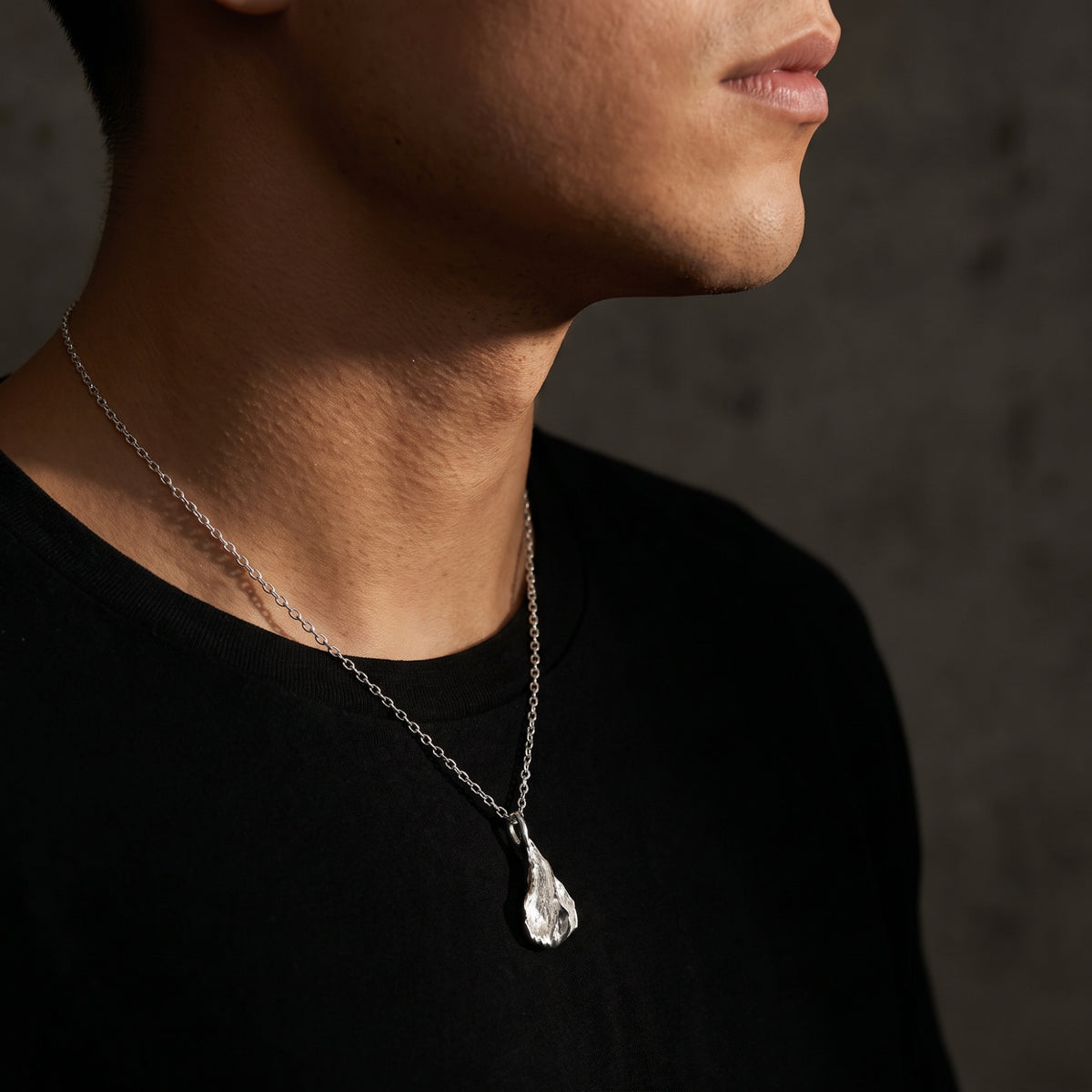 Angled profile view of a model wearing the silver petal pendant necklace over a black shirt.