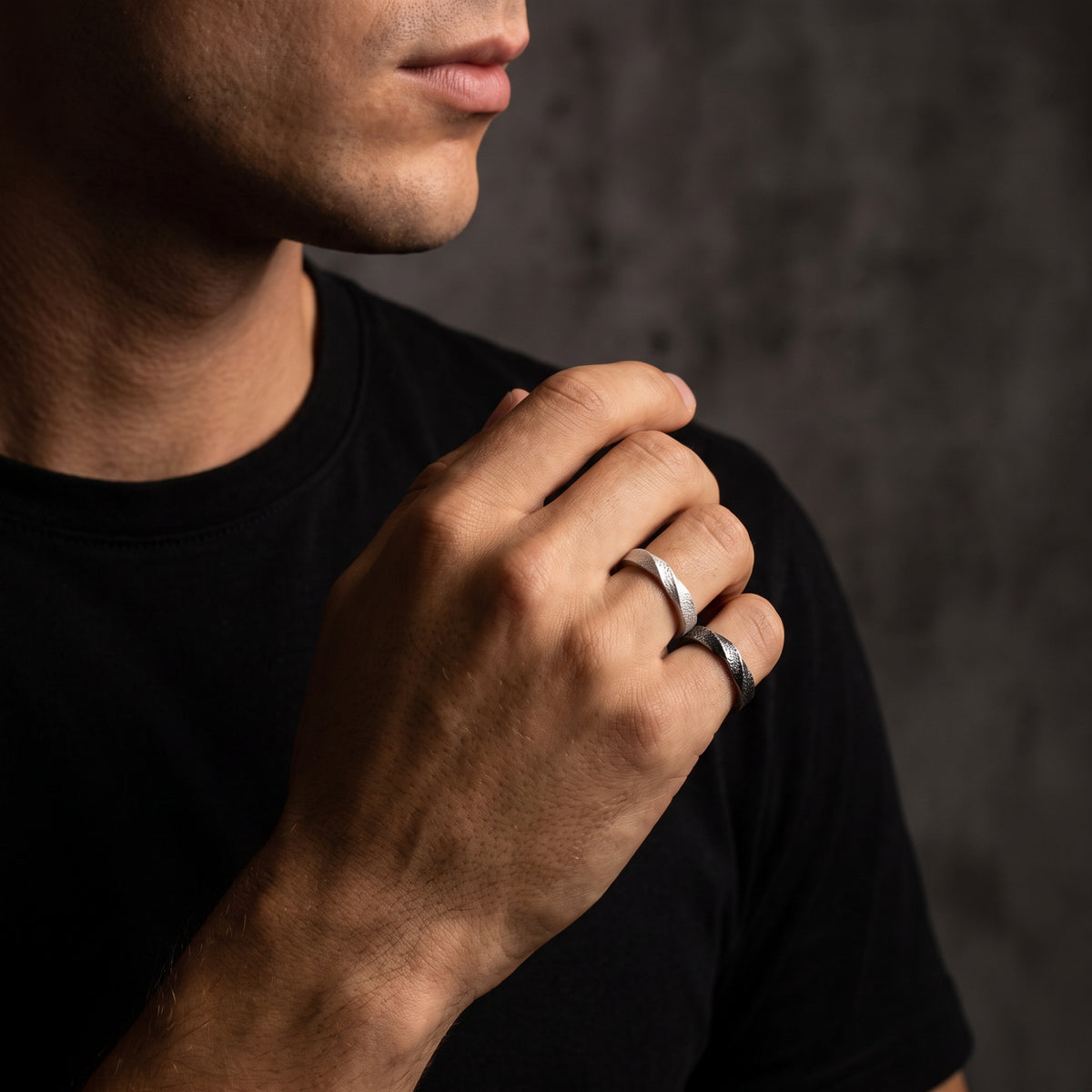 Man wearing light and dark textured open-band rings on adjacent fingers in a close-up portrait.