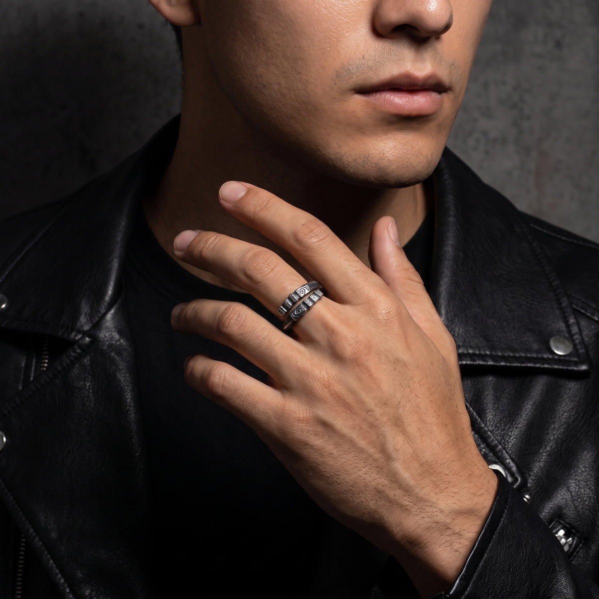 Man wearing a carved silver open-band ring on a finger while dressed in a black leather jacket.
