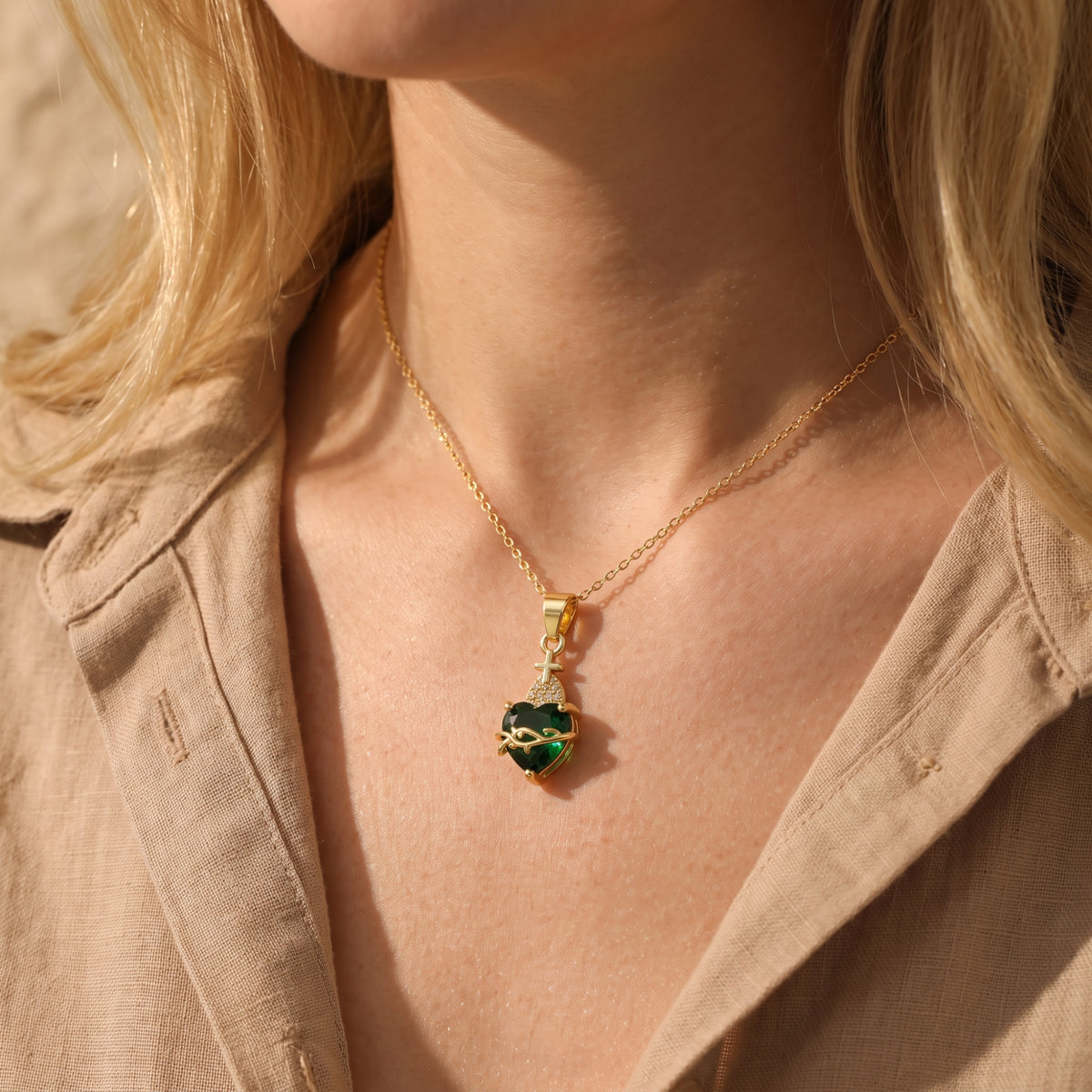 Gold-tone necklace with a green heart pendant worn over a tan shirt.