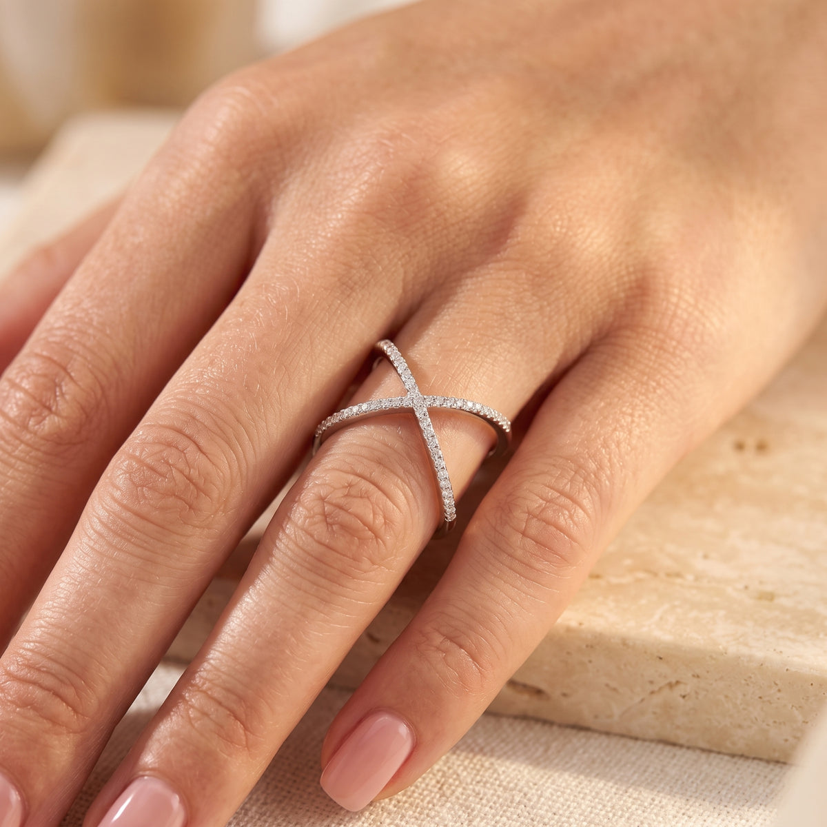 Close-up of a hand wearing the silver criss-cross ring with clear pavé stones along the overlapping bands.